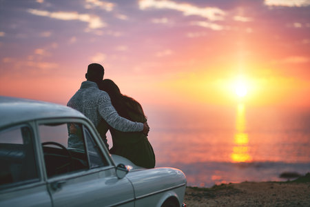 Watching the sun sunk into the sea. a young couple making a stop at the beach while out on a road trip.の写真素材