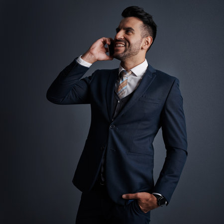 Keeping the business line of communication open. Studio shot of a stylish young businessman using a mobile phone against a gray background.の写真素材