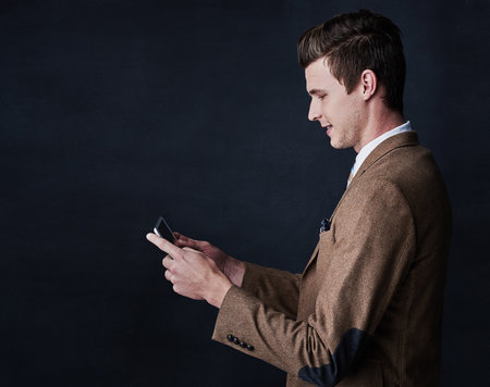 Ive all the right contacts. Studio shot of a young businessman using his cellphone against a dark background.の写真素材