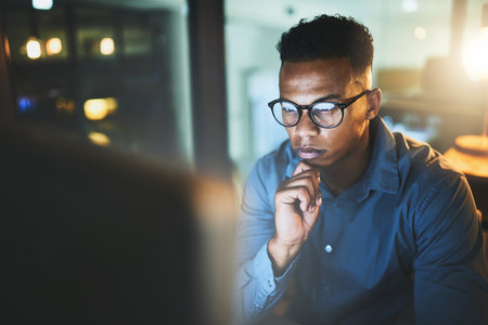 Giving it some thought. a handsome young businessman looking thoughtful while working late at night in a modern office.の写真素材
