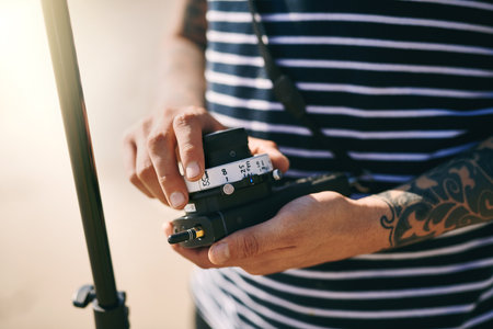 I have full control. Closeup of an unrecognizable man making a few adjustments on a state of the art video camera on a beach during the day.の写真素材