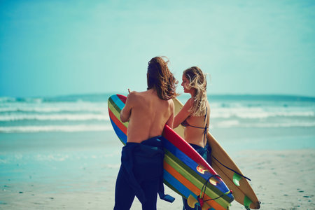 Let the waves take you away. a young couple walking on the beach with their surfboards.