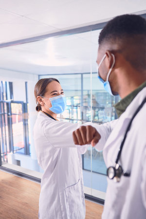 Safe greetings. two unrecognizable doctors wearing masks and elbow bumping while standing in the hospital.の写真素材