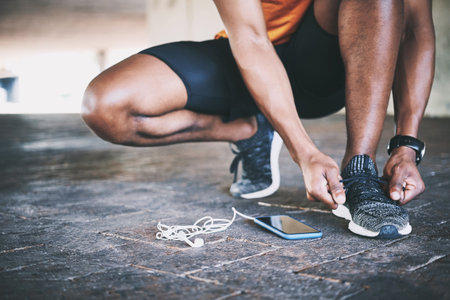 I dont get tied up in excuses. a man tying his shoelaces during a workout against an urban background.の写真素材