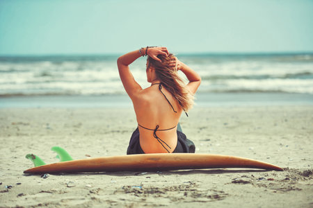The best thing to do on a summers day. a beautiful young woman going for a surf at the beach.の写真素材