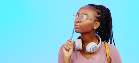 Black woman, thinking and gen z person with student vision and ideas in a studio copy space. Blue background, university students idea and headphones of a young female with glasses contemplating withの写真素材