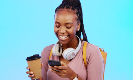 Phone, music and coffee with a black woman in studio on a gray background listening to the radio. Mobile, social media or headphones and a young female streaming an audio playlist with a drinkの写真素材