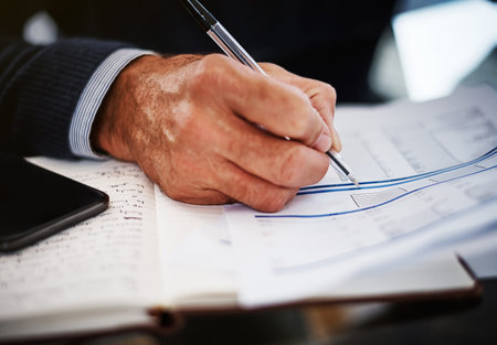 Staying on top of numbers and stats. a businessman writing on a document at his work desk.の写真素材