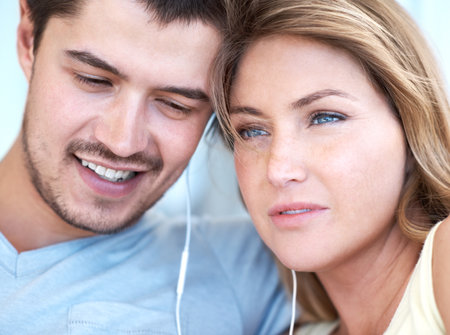 Listening to music together. Attractive young couple listening to music together on some earphones.の写真素材