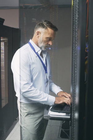 Securing a stable connection. a mature man using a laptop while working in a server room.の写真素材