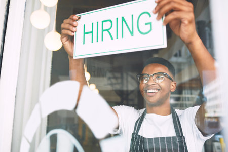 A growing business needs a growing team. a young man hanging up a hiring sign while working in a cafe.の写真素材