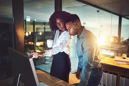 Ensuring the results meet the clients requests. two businesspeople working together on a computer in an office at night.の写真素材
