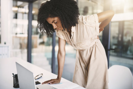 Stress has built up in her back. a young businesswoman experiencing back pain while working in a modern office.の写真素材