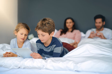 Mornings in our home. an adorable little girl and boy using a tablet together while their parents...