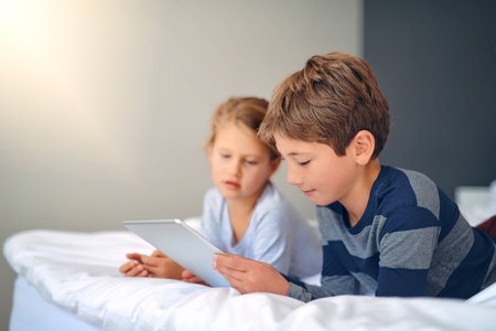 Discovering new apps together. an adorable little girl and boy using a tablet together while chilling on the bed at home.の写真素材