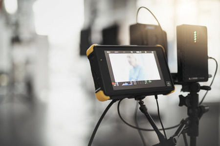 What we see behind the camera. Behind the scenes shot of videography recording equipment and a screen looking at a scene inside of a studio during the day.の写真素材