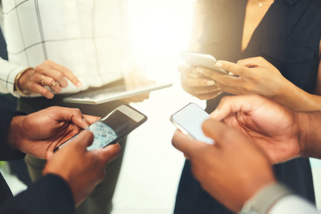 Matching their ideas in mobile form. Closeup shot of a group of businesspeople using their digital devices in synchronicity in an office.の写真素材