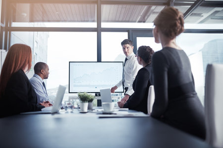 Hes an up and comer in the company. an executive giving a presentation on a monitor to colleagues in a modern boardroom.の写真素材