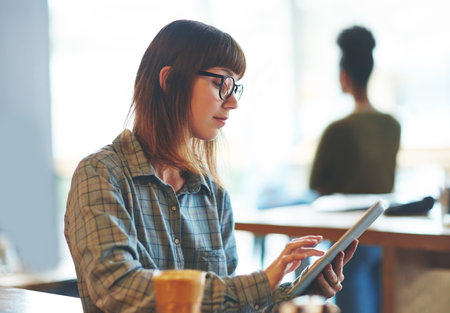 Browsing through her social media feeds. an attractive young woman using a digital tablet in a cafe.の写真素材