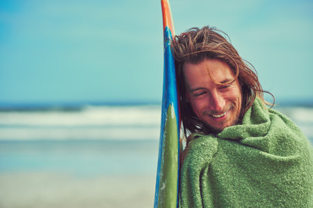 Surfing brings me so much joy. a young surfer leaning against his surfboard.の写真素材