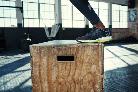 Jumping closer towards my fitness goals. an unrecognizable man doing jumping exercises on a wooden block in a gym.の写真素材