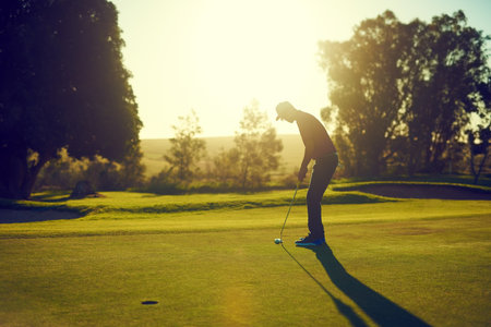 On course for a win. a young man hitting the ball out of the bunker during a round of golf.の写真素材