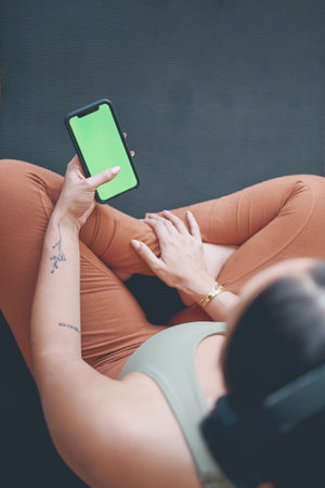 Technology is like your own personal trainer. High angle shot of a young woman wearing headphones and using a cellphone while exercising at home.の写真素材