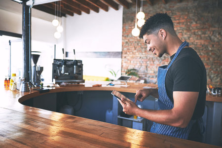 Another day, another five star review. a confident young man using a digital tablet while working in a cafe.の写真素材