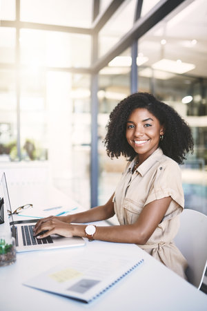 Success is a doing word. Portrait of a young businesswoman using a laptop at her desk in a modern office.の写真素材