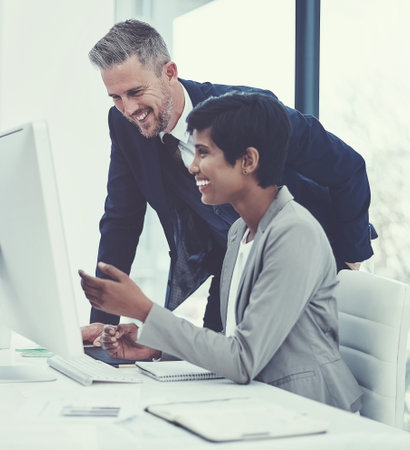 The partnership that produces results. a businesswoman and businessman using a computer together at work.の写真素材