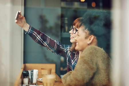 Every snap taken is a memory stored forever. two young friends taking a selfie together in a cafe.の写真素材