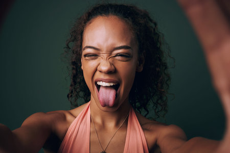 Selfie, tongue out and young woman in studio with facial, expression or personality on green...