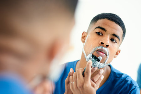 Hair removal, face and shaving with man in bathroom for grooming, morning routine and cleaning. Skincare, razor and self care with male person in mirror at home for facial, beard and hygieneの写真素材