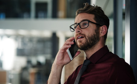 Can you talk. a young businessman using a mobile phone in a modern office.の写真素材