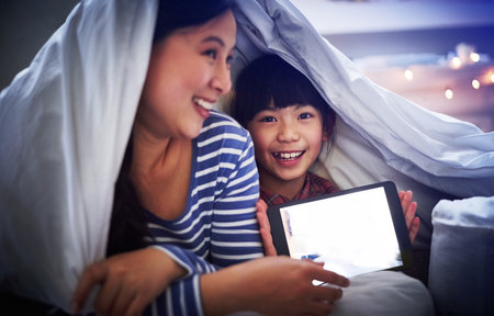 Look what were watching. an attractive young woman and her daughter using a digital tablet while lying under the covers.の写真素材