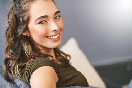 Im in good company all by myself. Portrait of a beautiful young woman relaxing on her sofa at home.