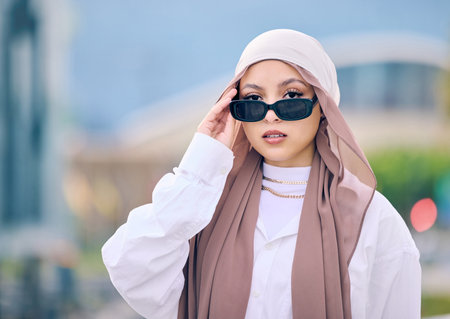 Portrait, fashion or sunglasses with a muslim woman in saudi arabia wearing a cap and scarf for contemporary style. Islam, faith and hijab with a trendy young arab person posing outside in shadesの写真素材