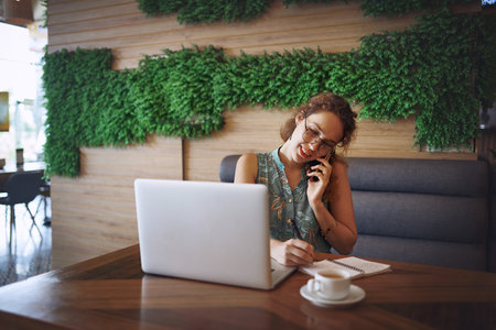 An office away from the office. a young woman using a laptop and smartphone while working at a cafe.の写真素材