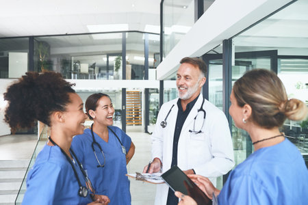 Always make time for a laugh. a handsome mature doctor standing with his nurses and having a discussion in the clinic.の写真素材