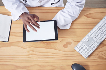 Research never ends in a medical field. High angle shot of an unrecognizable doctor sitting alone in his office at the clinic and using his digital tablet.の写真素材