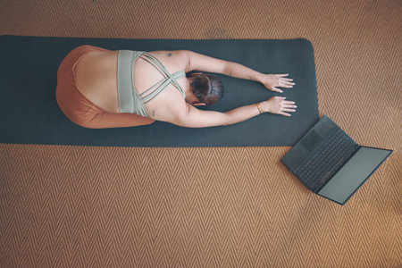 The benefits of yoga are beyond the mat. High angle shot of a young woman using a laptop while practising yoga at home.の写真素材