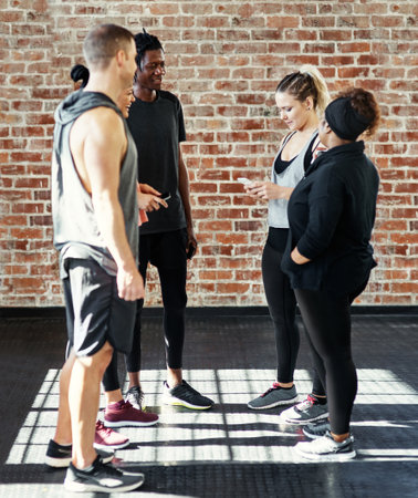Take two. a cheerful young group of people standing in a circle and having a conversation before a workout in a gym.の写真素材