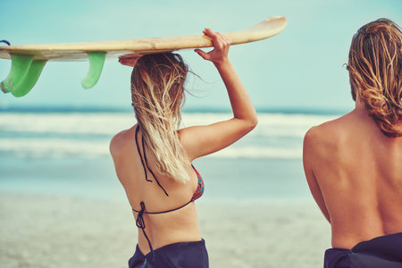 Off to the next ride. a young couple walking on the beach with their surfboards.