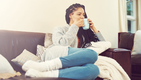Coffee is my survival juice. a young woman enjoying a cup of coffee in her living room.