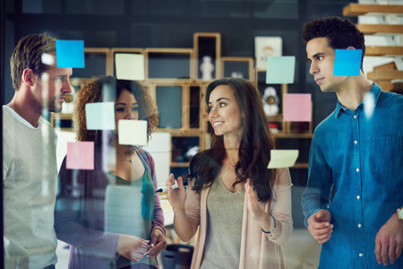 Theyre visionaries who are keen on big transformations. a group of young designers brainstorming with notes on a glass wall in an office.の写真素材