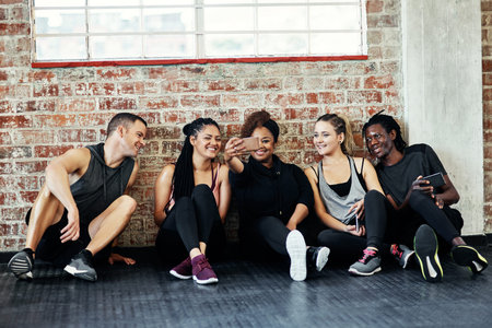 Fun times in the gym. a cheerful young group of people sitting down on the floor and taking a self...