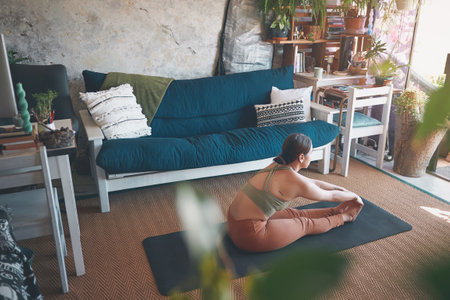 Enhance your feeling of wellbeing. a young woman touching her toes while exercising at home.の写真素材