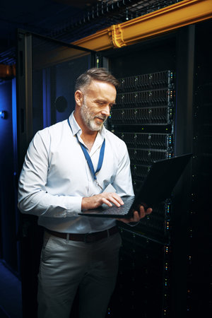 Lets see if this works now. a mature man using a laptop while working in a server room.