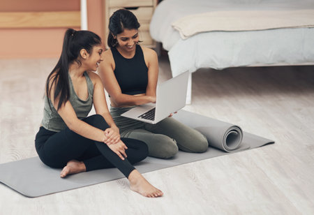 Women, laptop and exercise together at home with happiness, health and wellness. Indian sisters or female friends in a lounge for online class, yoga website or fitness workout video with a partnerの写真素材