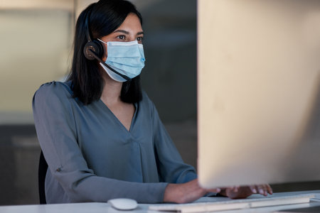 Call center, woman and face mask at computer for customer service, telemarketing sales and CRM consulting in office. Female agent, desktop and covid safety for online telecom advice, support and helpの写真素材
